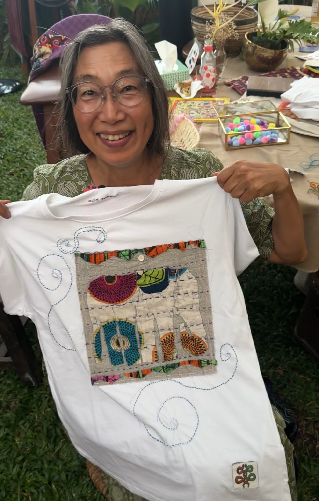 Woman holding a white garment with a colorful patchwork design outdoors a workshop by Acid Moons studio in Goa.
