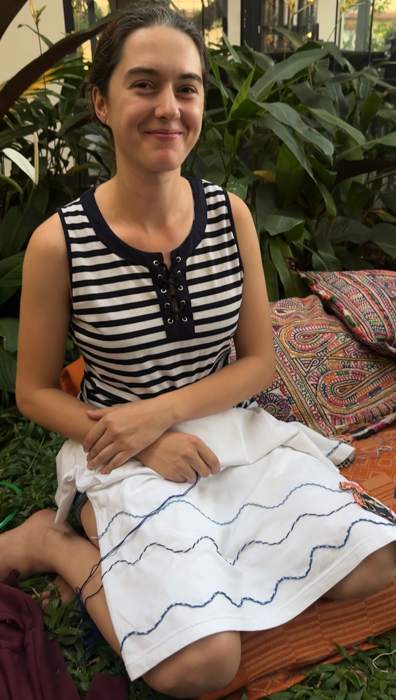 Woman sitting outdoors with plants in the background and embroidering for Acid Moons workshop in Goa