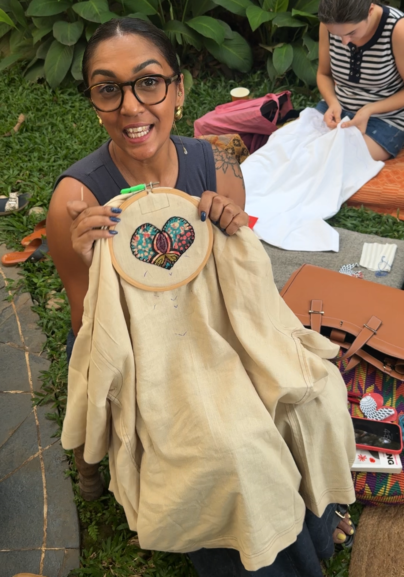 Woman holding a beige garment with a heart design, standing outdoors with greenery in the background a workshop by Acid Moons studio in Goa.
